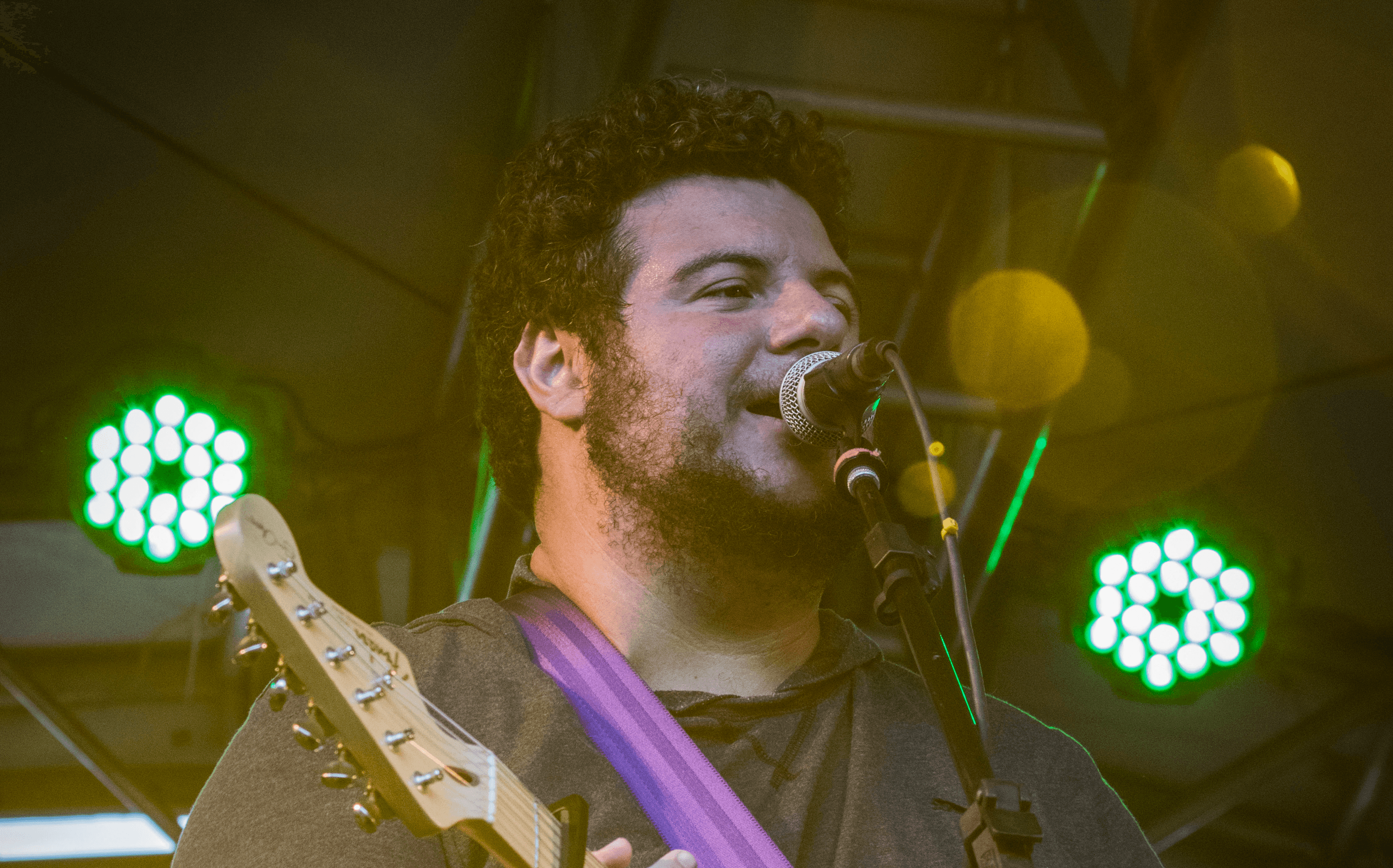 International blues guitarist singing into a microphone and playing guitar during a live performance.