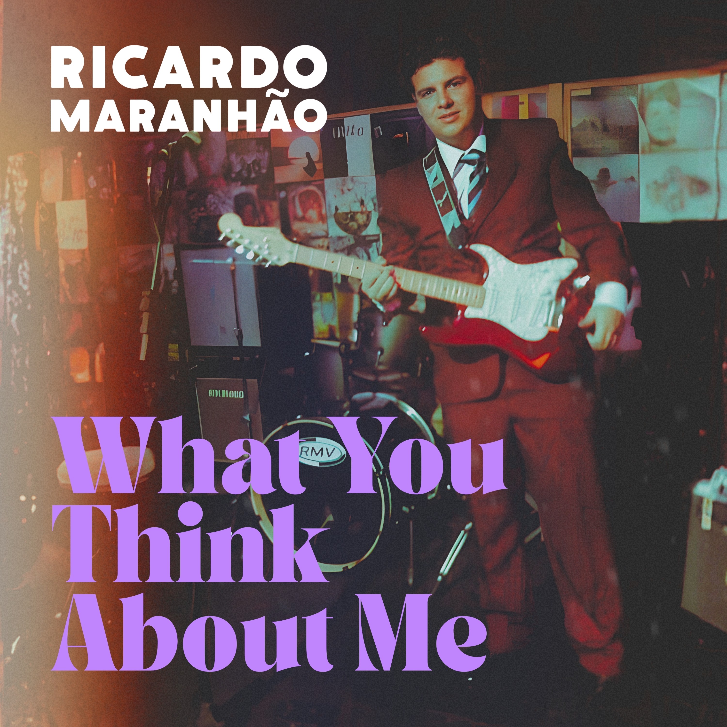 Cover art for the upcoming music release, featuring the artist holding a guitar, wearing a burgundy suit, in front of speakers, microphones, and visual elements of the band.