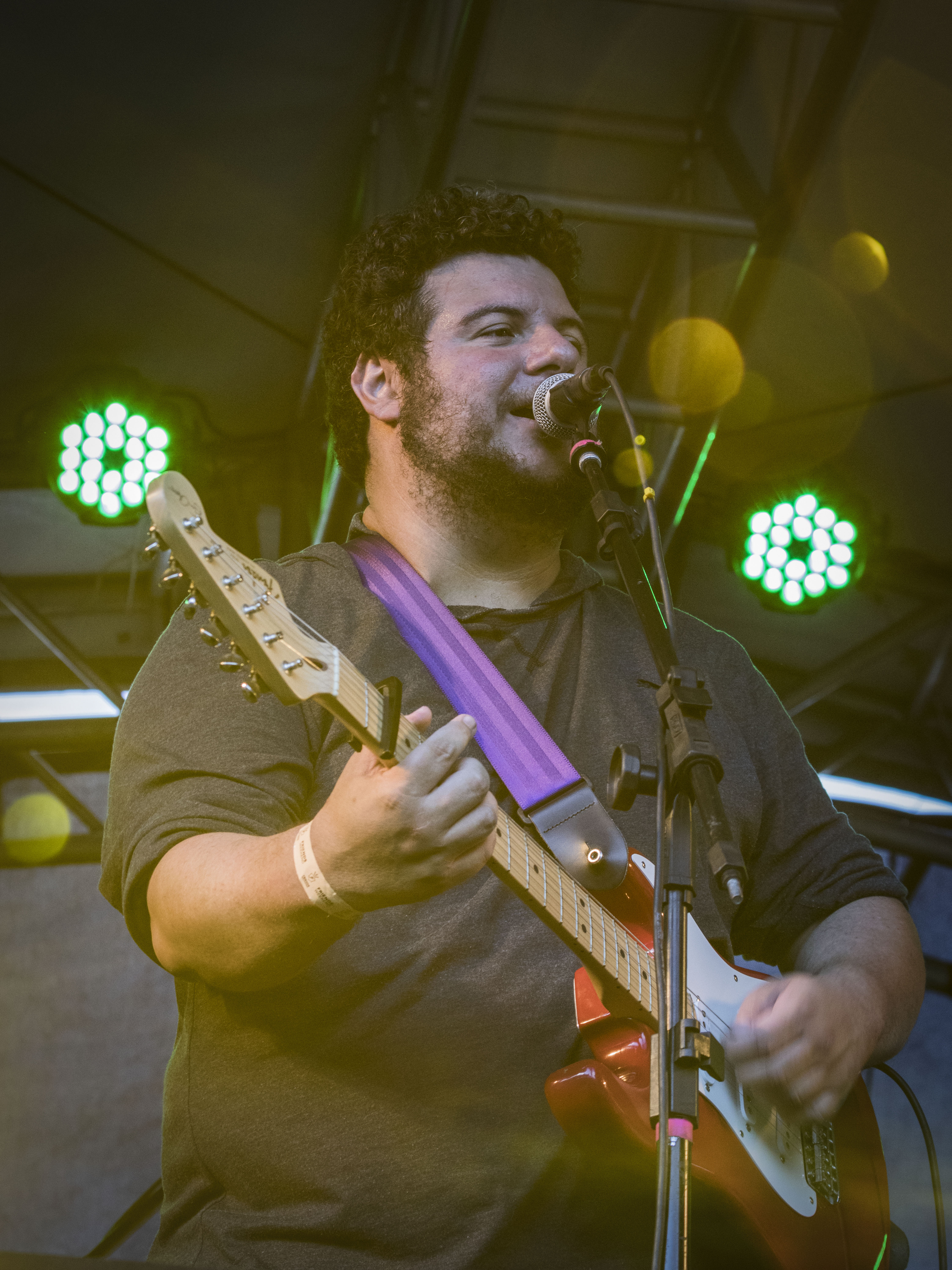 International blues guitarist singing into a microphone and playing guitar during a live performance.